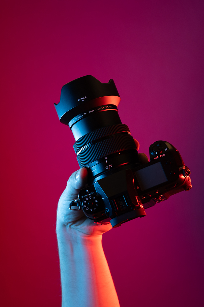 studio shot of a hand only holding a digital camera with red background